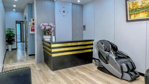 A modern hotel room with a wooden floor, a massage chair, a black sofa, a chandelier, and a painting on the wall. - Ann Apartment (Hai Phong)