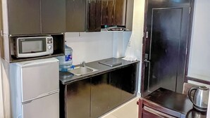 A compact kitchen with dark cabinets, a microwave, a refrigerator, and a sink. - Ann Apartment (Hai Phong)