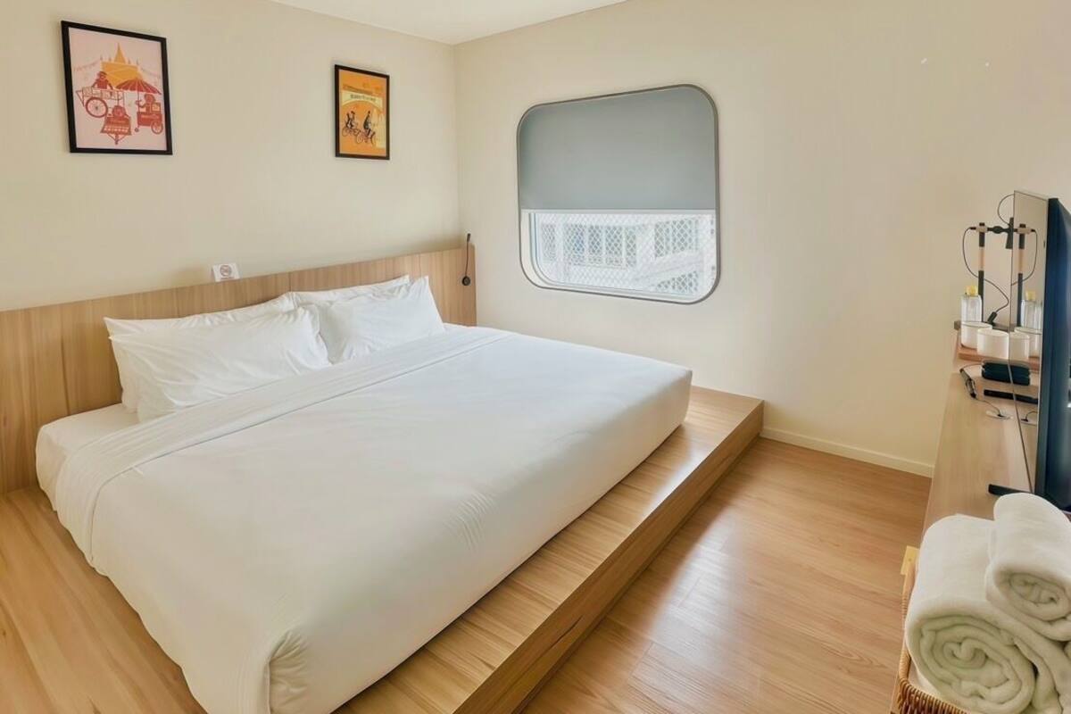 Ein schlicht eingerichtetes Schlafzimmer mit einem großen Bett, einem kleinen Fenster und einem Fernseher auf einem Holzboden.