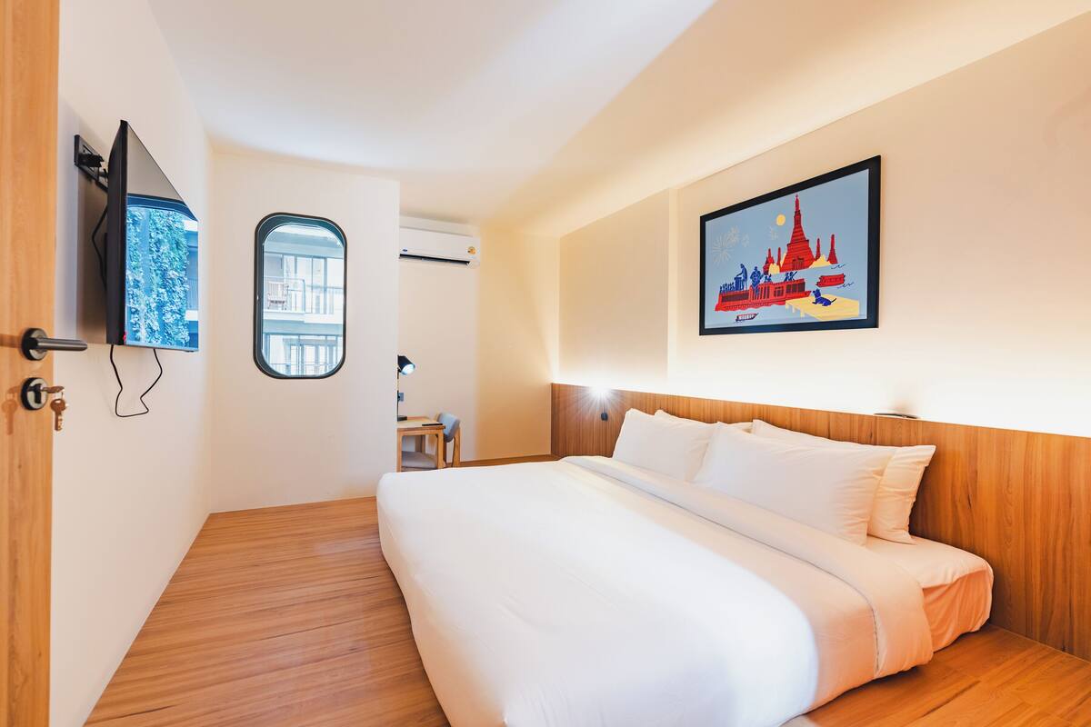 Ein Hotelzimmer mit Bett, Fernseher, Fenster und einem Wandbild.