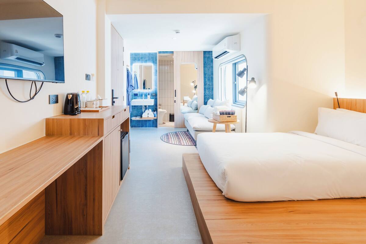 Ein modernes Hotelzimmer mit einem hölzernen Bett, einem Schreibtisch und einem durch eine offene Tür einsehbarer Badezimmer.
