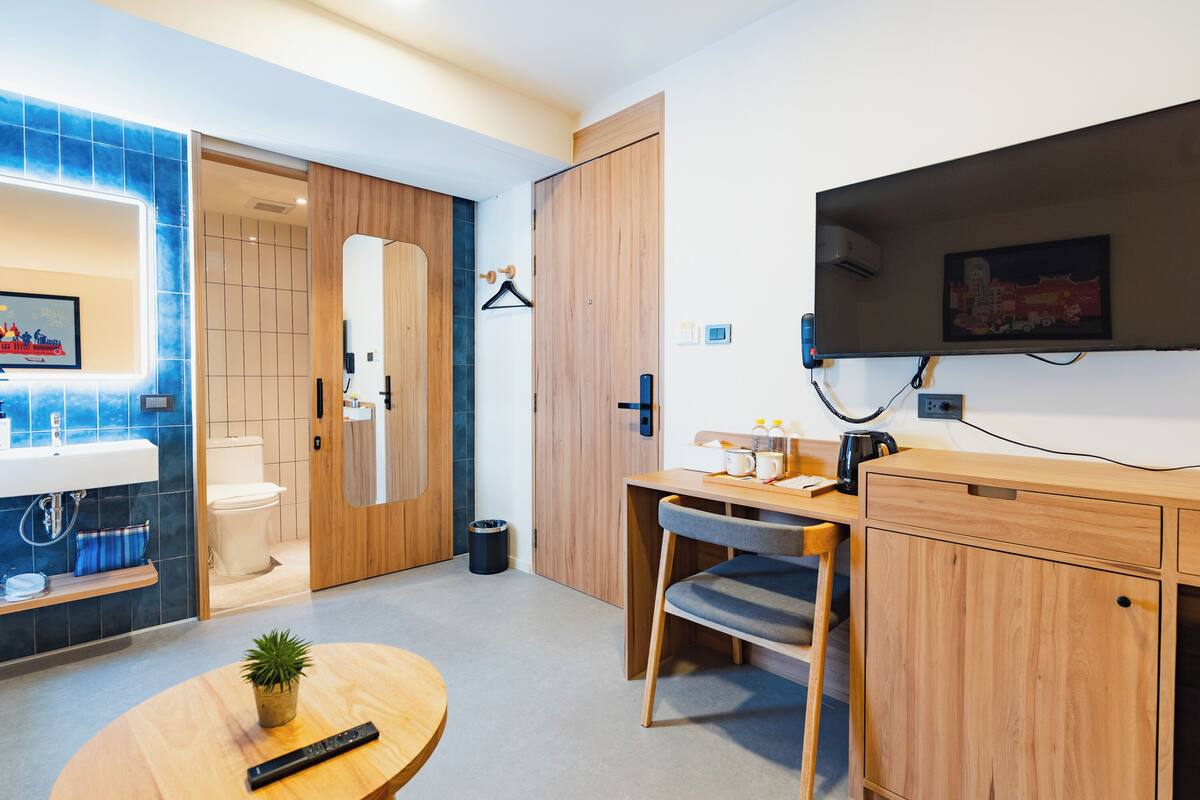 Ein modernes Badezimmer mit Waschbecken, Toilette und Spiegel. Ein Holztisch mit Stuhl und ein kleiner Tisch mit Pflanze sind ebenfalls vorhanden.