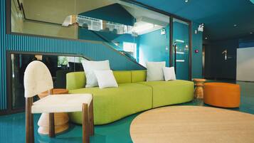 A modern interior with a green sofa, white cushions, a wooden chair, and a round wooden table.