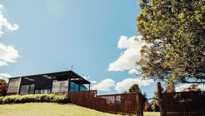 A modern house with large windows, a sloped roof, and a fenced yard. - A Romantic Escape in Nature’s Embrace (Bullarto South)