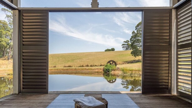 A room with a large window overlooking a calm lake and grassy landscape. - A Romantic Escape in Nature’s Embrace (Bullarto South)