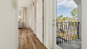 Ein Korridor mit Holzboden, der zu einem Balkon mit schwarzer Geländer führt.