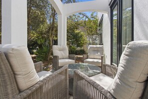 A covered outdoor seating area with wicker furniture and a glass table.