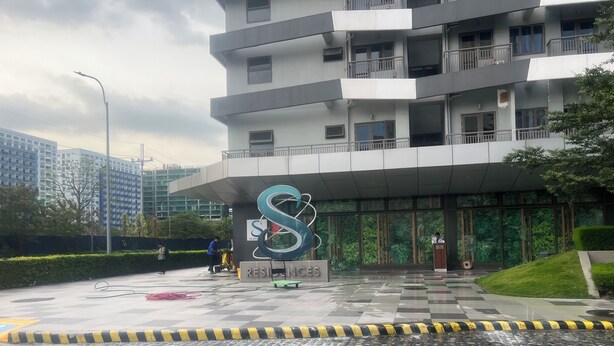 Un edificio moderno con un amplio logotipo en forma de S, una entrada protegida por una reja y un césped cuidado.