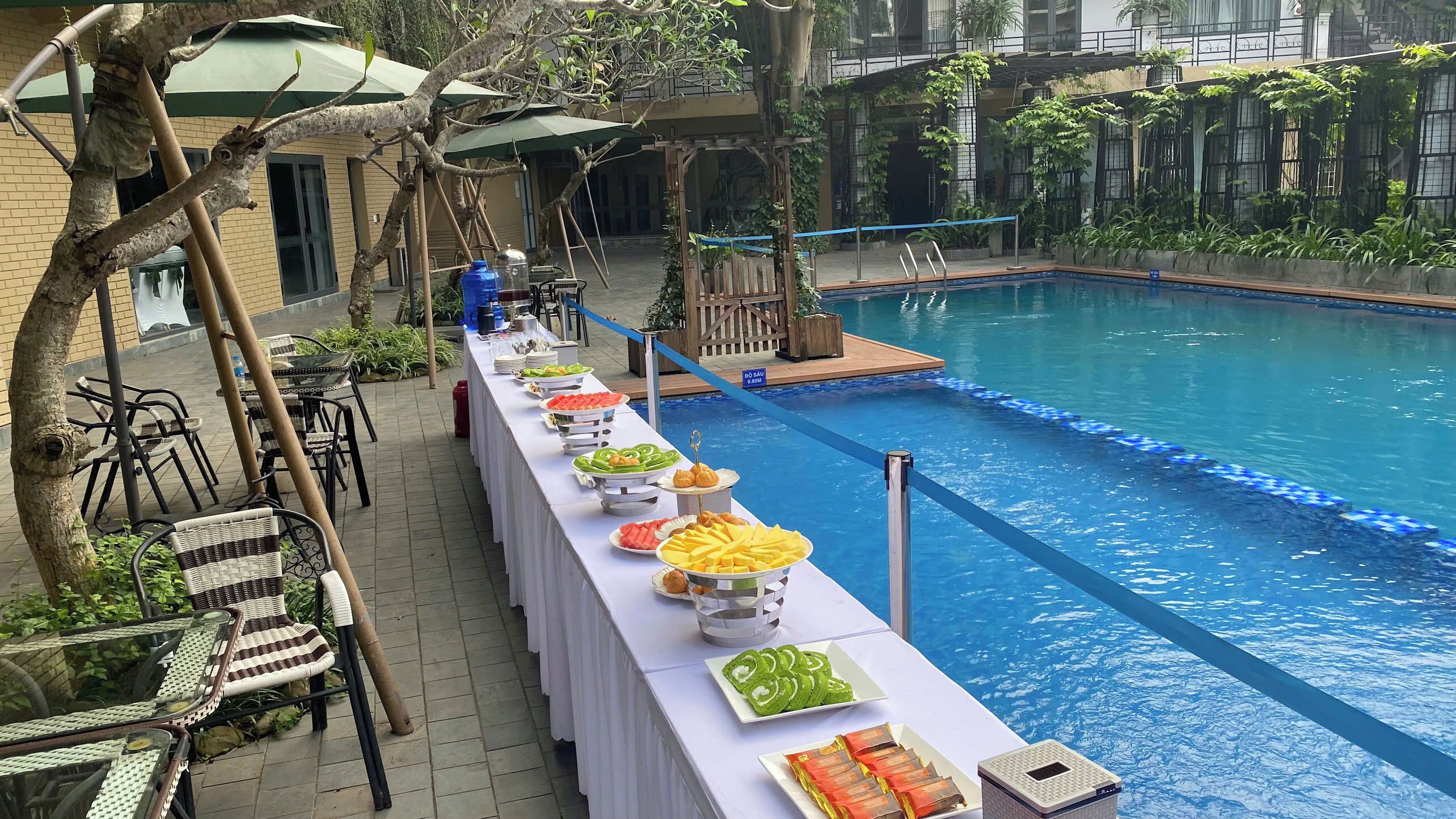 Un buffet est installé au bord de la piscine, proposant divers plats, et la piscine elle-même est bordée de carrelage bleu.
