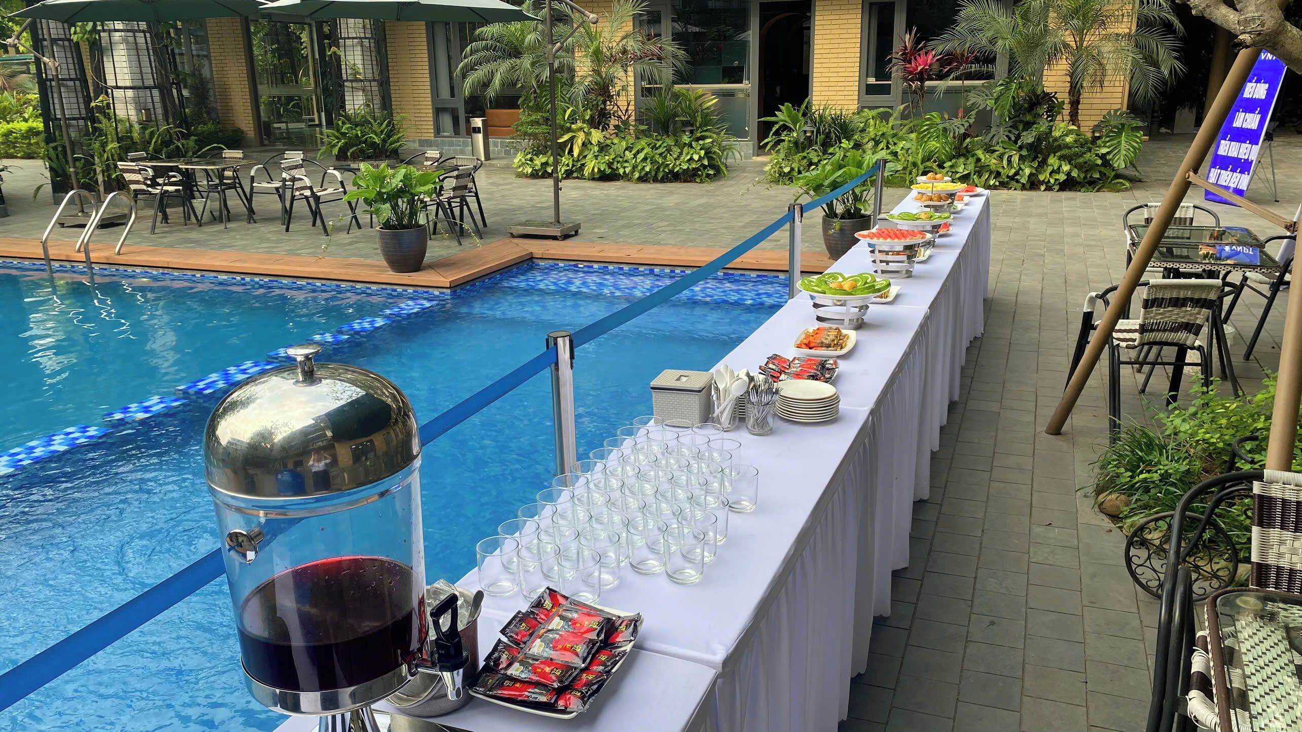 Ein Poolbuffet mit langem Tisch, Esstischen und einem Pool mit blauem Mosaikrand.