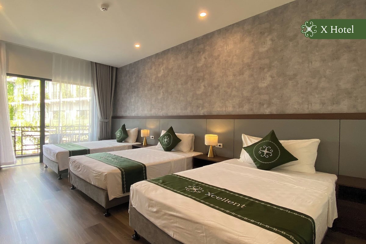 Ein Hotelzimmer mit zwei Betten, einem Schreibtisch und Blick auf Grünflächen.