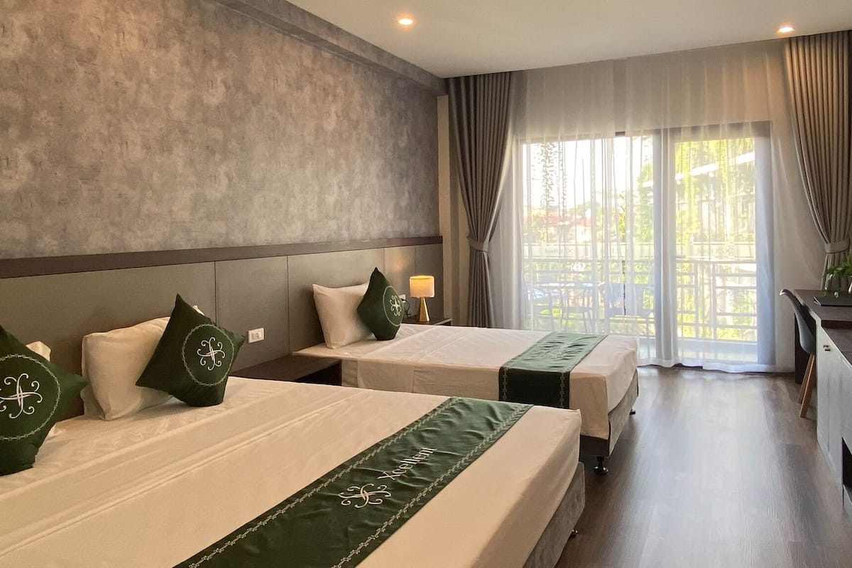 Ein Hotelzimmer mit zwei Betten, einem Fernseher, einem Schreibtisch und Balkonblick.