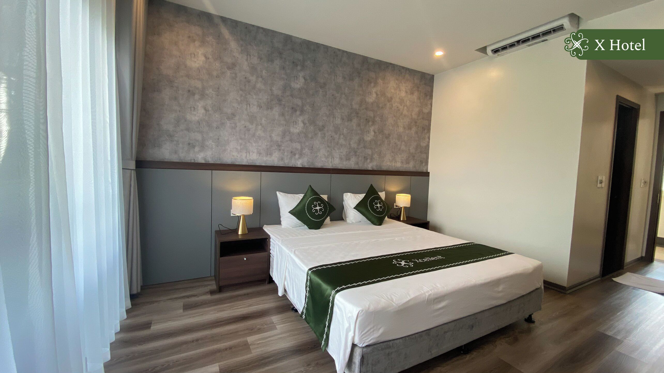 A hotel room with a large bed, two nightstands, a headboard, and a green bed runner.