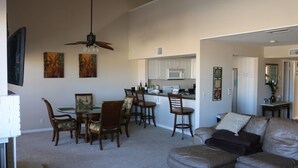 A spacious living area with a leather sofa, a dining table with chairs, and a kitchen in the background.