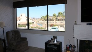 A room with a large window offering a view of a building and palm trees. There is a chair, a small table with a printer, and a fireplace.