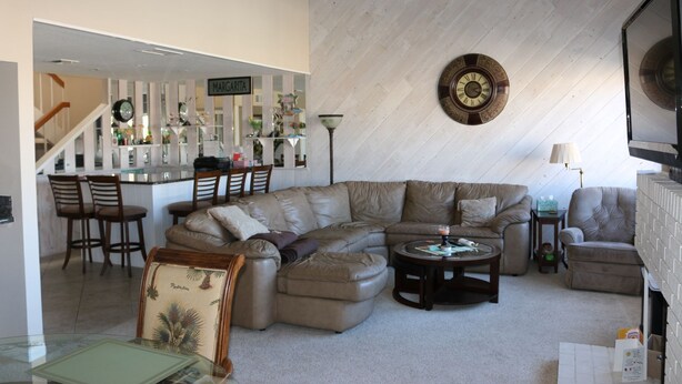 A spacious living area with a large L-shaped sectional sofa, a coffee table, and a dining area with chairs and a kitchen counter.