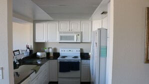 A compact kitchen with white cabinets, a microwave, a stove, and a refrigerator.