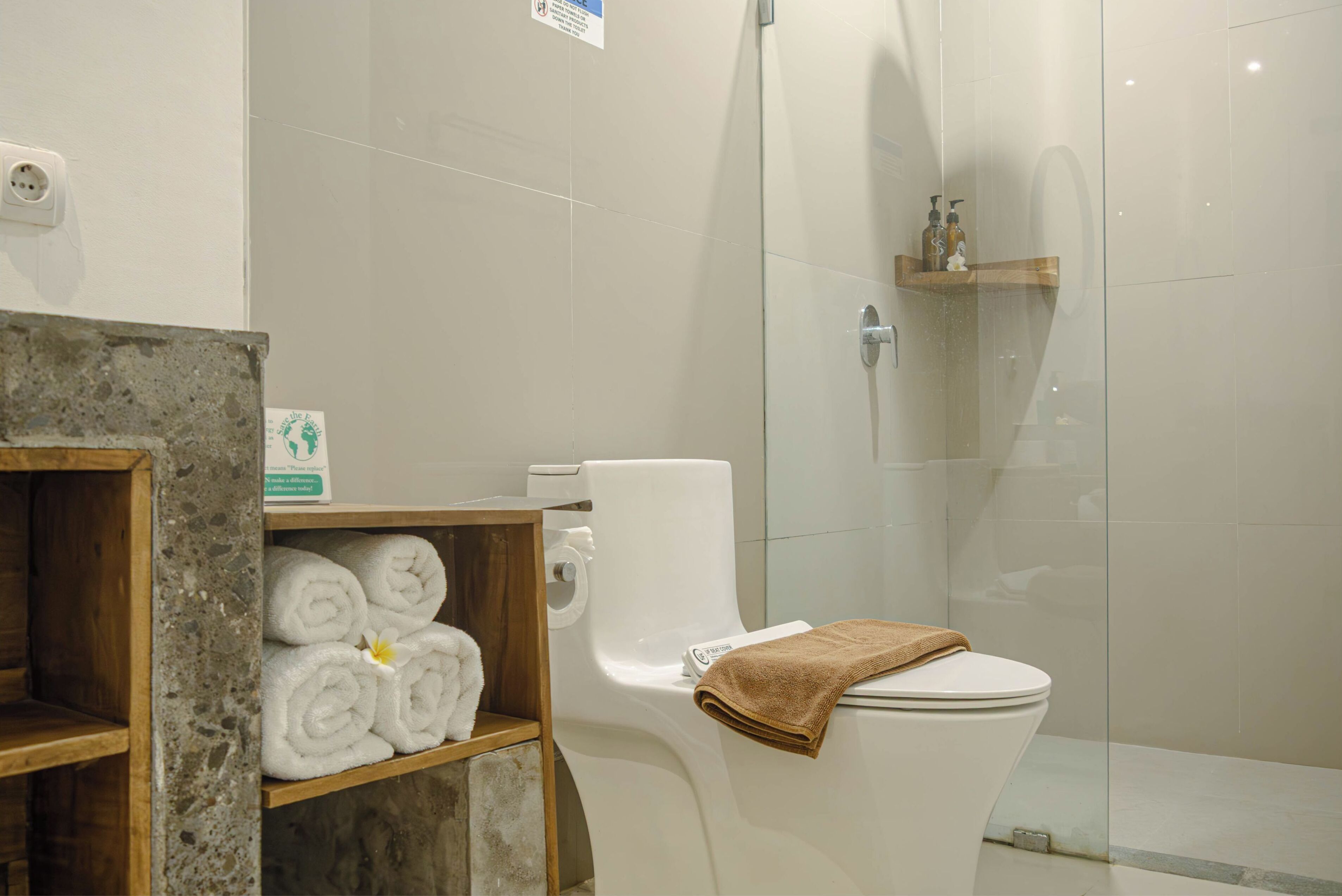 A modern bathroom with a toilet, a glass shower enclosure, and a shelf with neatly rolled towels.