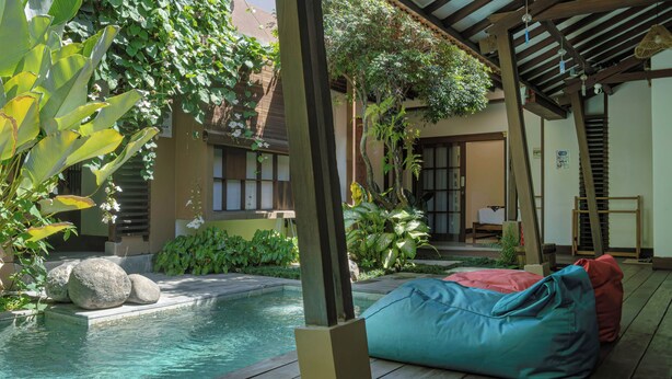 Ein Poolbereich mit Holzterrasse, blauem Sitzsack und einem Gebäude im traditionellen Stil mit Ziegeldach.
