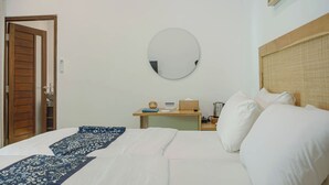 Ein Hotelzimmer mit einem Bett, einem runden Spiegel, einer Holztür, einem kleinen Tisch mit einer Uhr und einem Nachttisch mit einer Lampe.