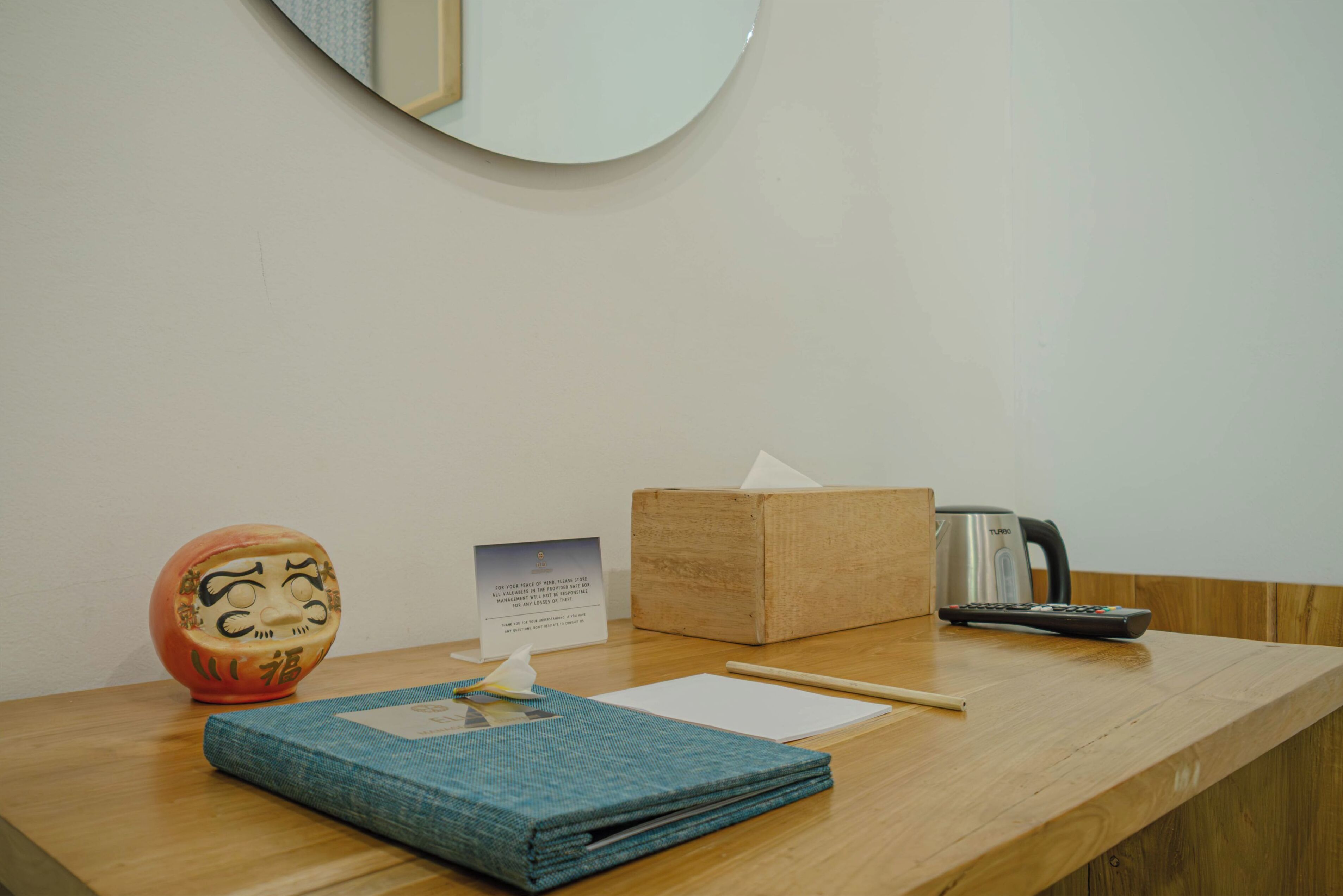 A wooden table with a tissue box, a remote control, a tissue, a pen, and a decorative item.