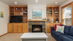 A living room with a fireplace, wooden shelves, a television, and a blue sofa. - SeaEscape: Cute home, dog ok, near beach & pub! (Pacific City)