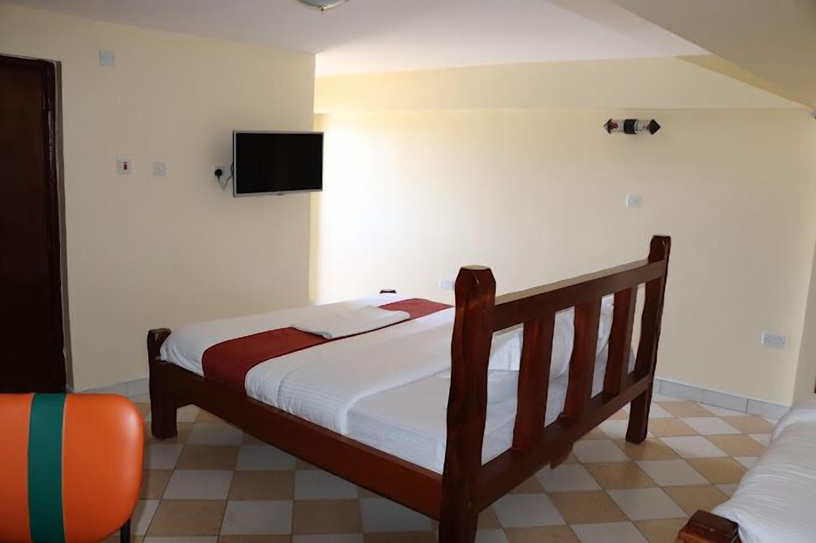 A room with a single bed, a television mounted on the wall, and a checkered floor.