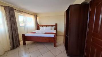 Una habitación de hotel con cama, cortinas, un armario de madera y suelo de baldosas.