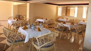 A dining area with multiple tables and wicker chairs, each with a white tablecloth and orange napkins. - Helsinki Hotel Nyamira (Nyamira)