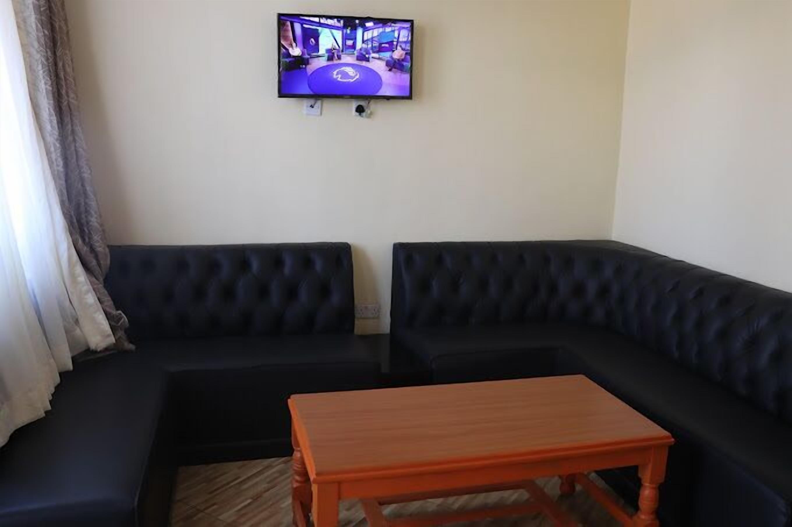 Una sala de estar con un sofá de cuero negro, una mesa de centro de madera y un televisor de pantalla plana en la pared.