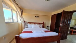 A hotel room with a wooden bed, a large window with curtains, a wardrobe, and a tiled floor. - Helsinki Hotel Nyamira (Nyamira)
