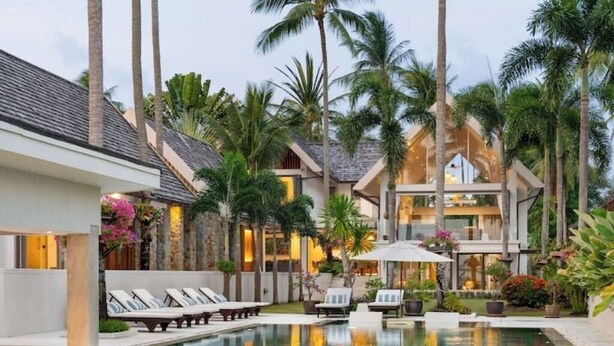 A resort with a swimming pool, lounge chairs, palm trees, and a modern building with large windows. - Best Family Beachfront Villa Koh Samui |Chef| Staff|JetSkis|Pool|No Hidden Fees| (koh samu)