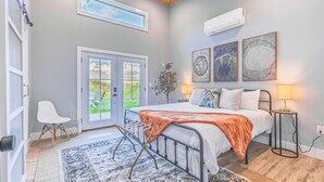 A bedroom with a bed, a chair, a small table, a window, and a door.