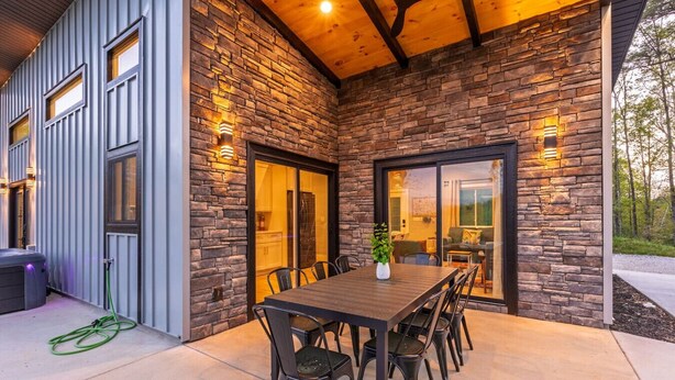 A modern outdoor dining area with a stone wall, a wooden ceiling, and a large table with chairs.