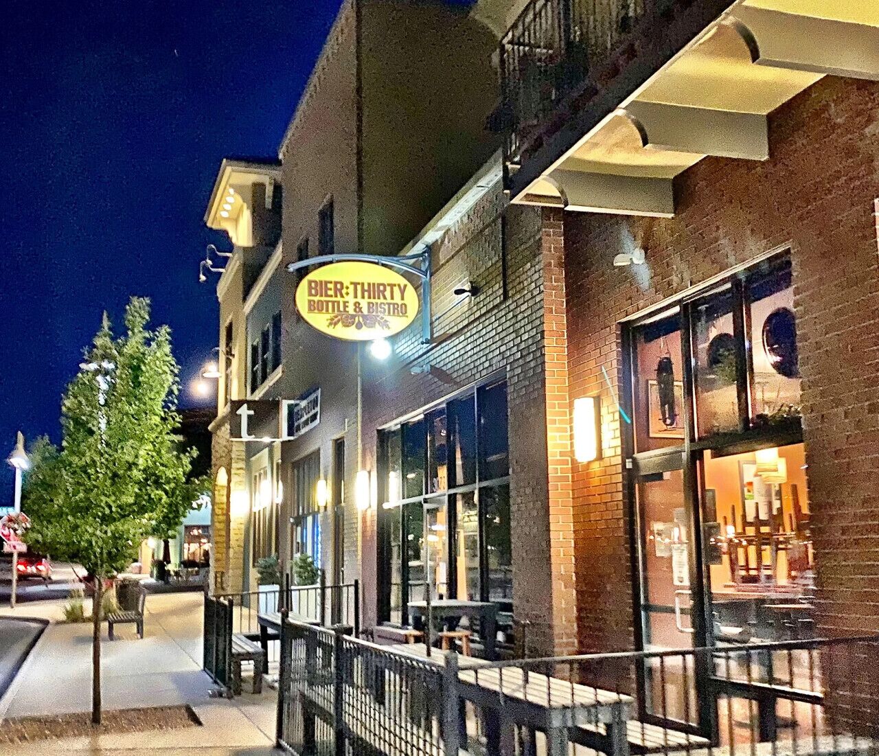 A building with a sign for 'Bier-THIRTY Bottle & Bistro' and a sidewalk with a tree and benches.