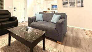 A living room with a dark grey sofa, two blue cushions, a marble coffee table, and a dining table with chairs. - Seaside Escape | Walk to Downtown Meridian • Garage • Pet Friendly • Fenced Yard • Near Roaring Springs & Wahooz (Meridian)
