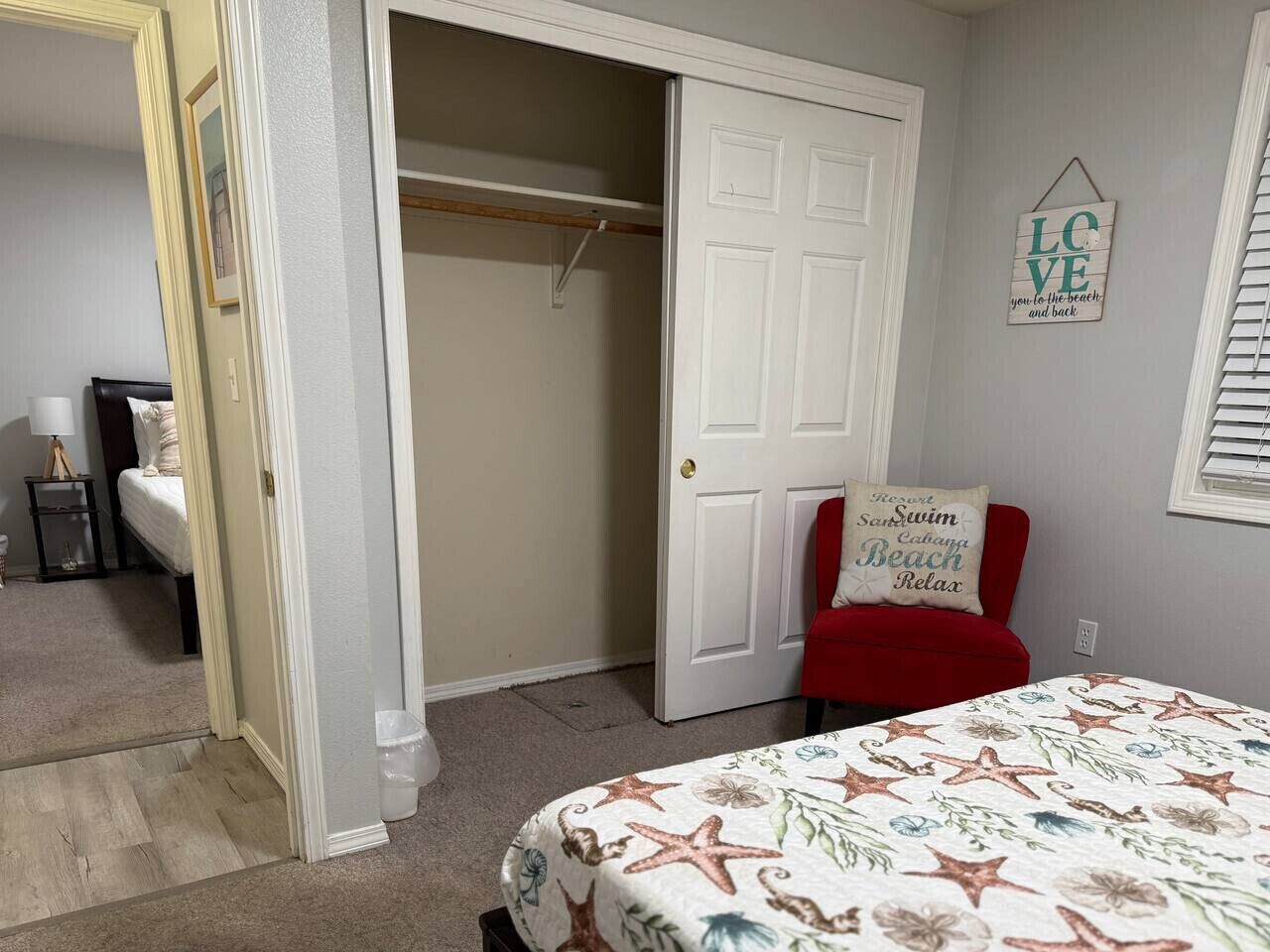 A bedroom with a bed, a closet, and a red chair with a beach-themed pillow.