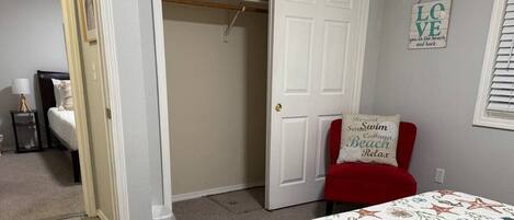A bedroom with a bed, a closet, and a red chair with a beach-themed pillow.