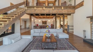 Un amplio salón con una escalera de madera, un gran conjunto de sofás y un comedor al fondo.