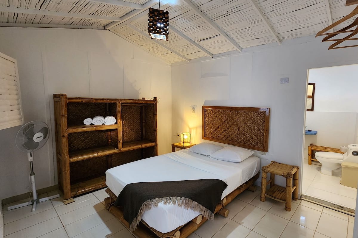 Une chambre à coucher comprenant un lit, une table de chevet, une lampe, une armoire, ainsi qu’une salle de bain avec des toilettes et un lavabo.