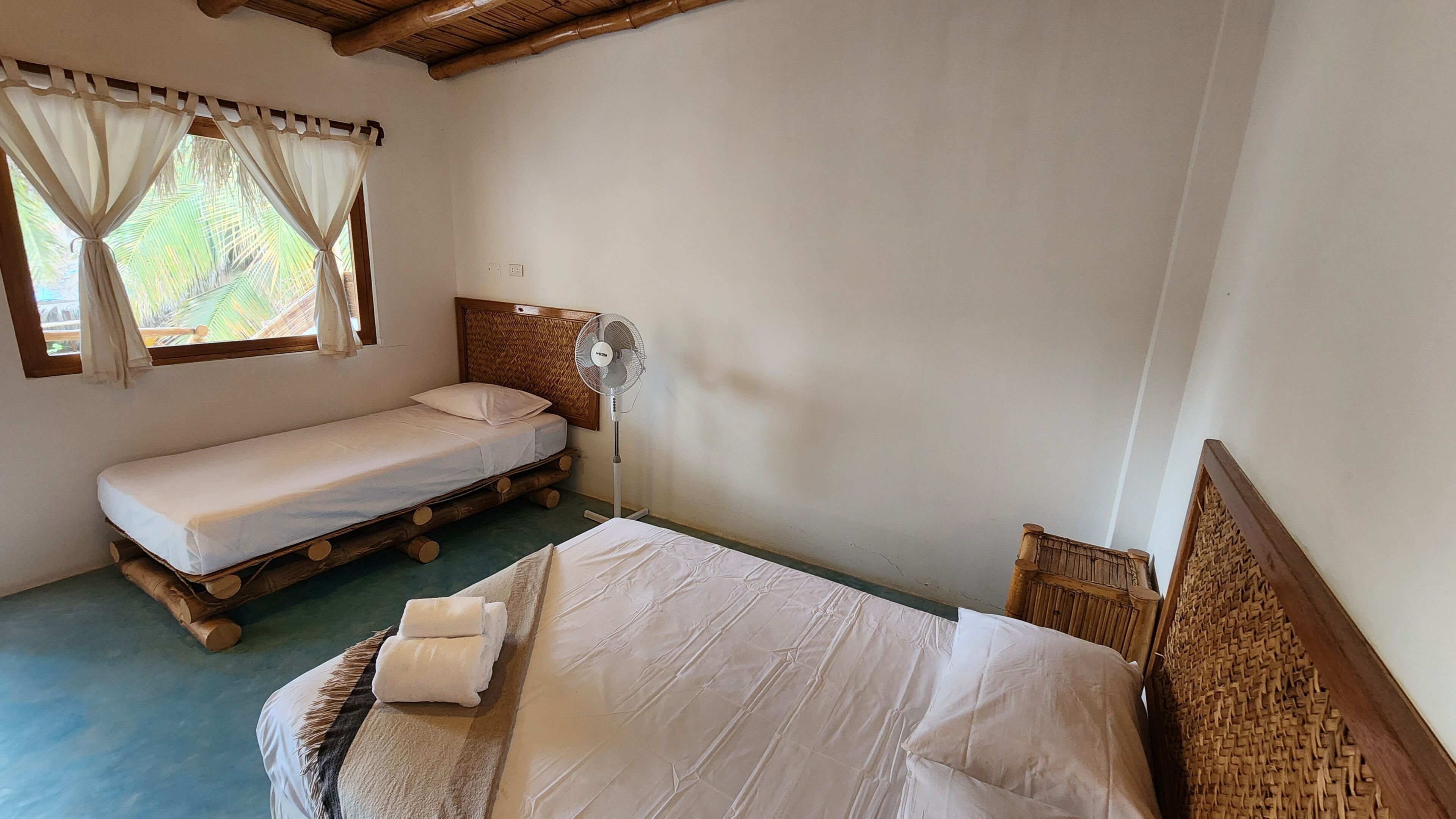 Una habitación individual con cama, ventilador y ventana con cortinas.