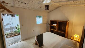 Una habitación con cama, repisa de madera, ventilador y ventana.