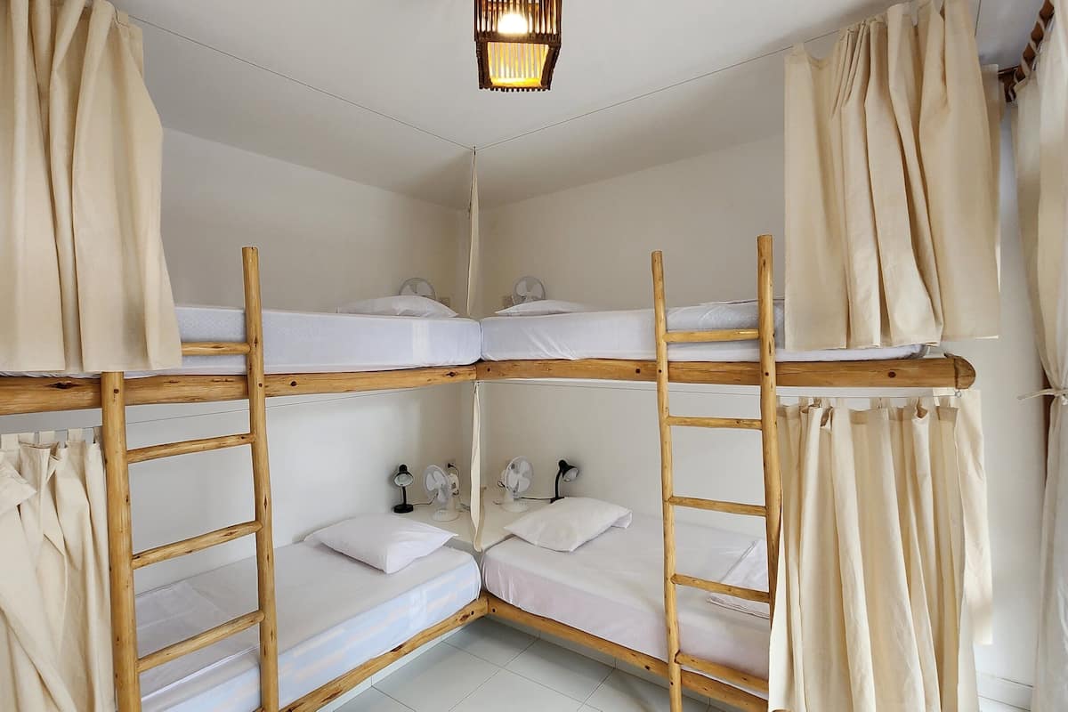 Une chambre avec un lit superposé doté de barrières en bois, de draps blancs et d’un ventilateur de plafond.