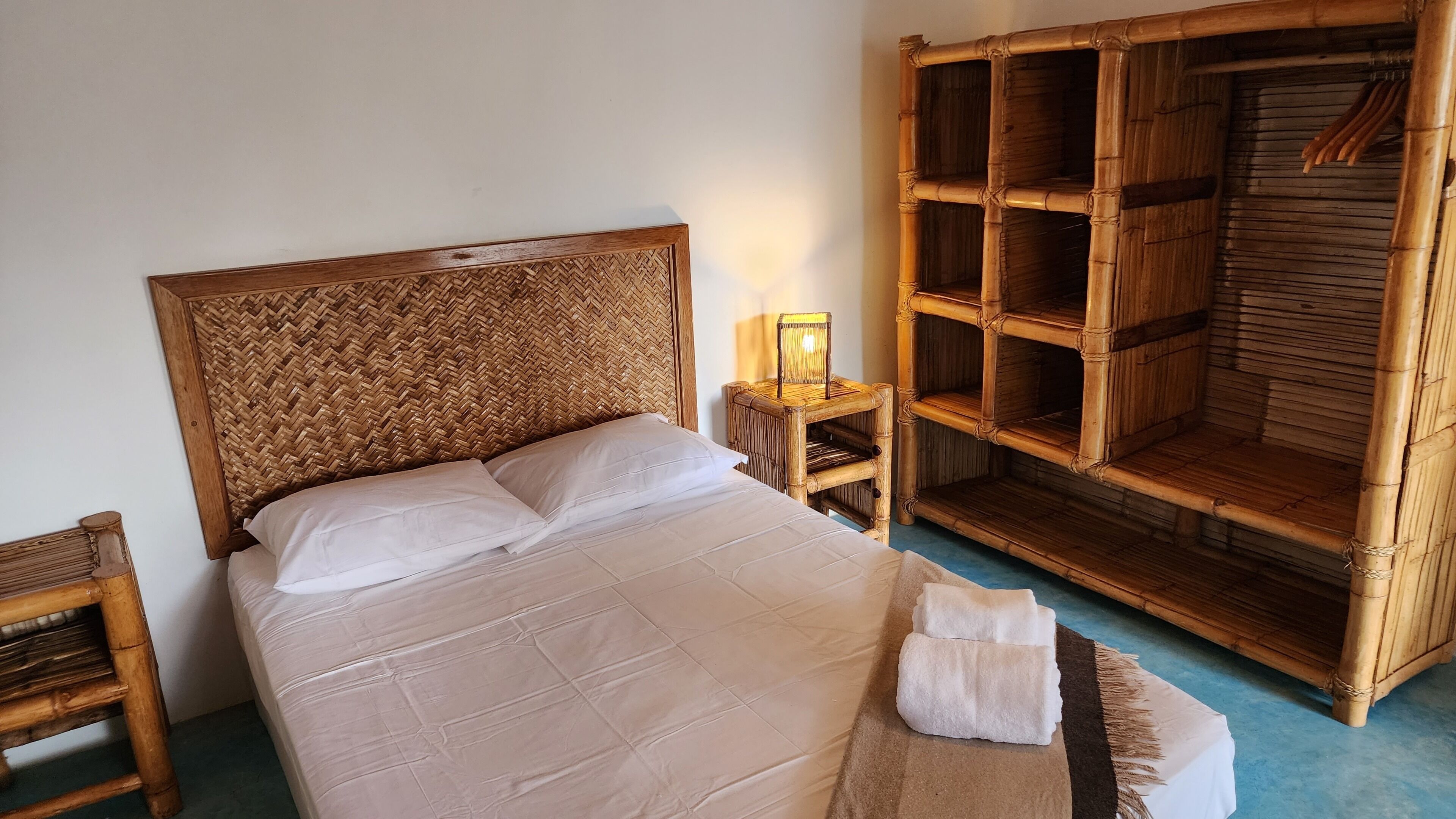 A bed with a woven headboard, a bedside table with a lamp, and a wooden wardrobe.