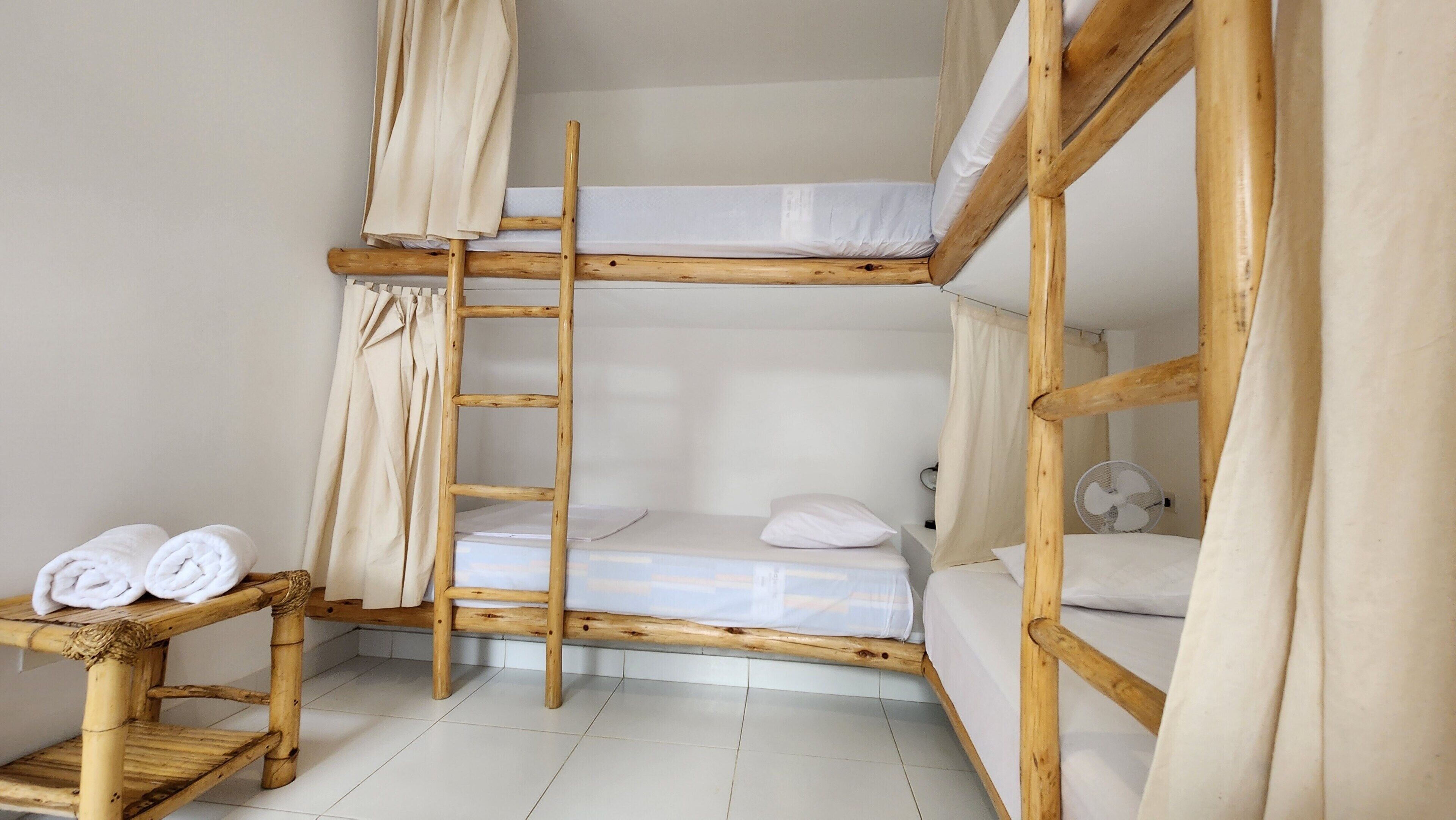Une chambre avec un lit superposé, une échelle en bois, une petite table avec des serviettes et un ventilateur.