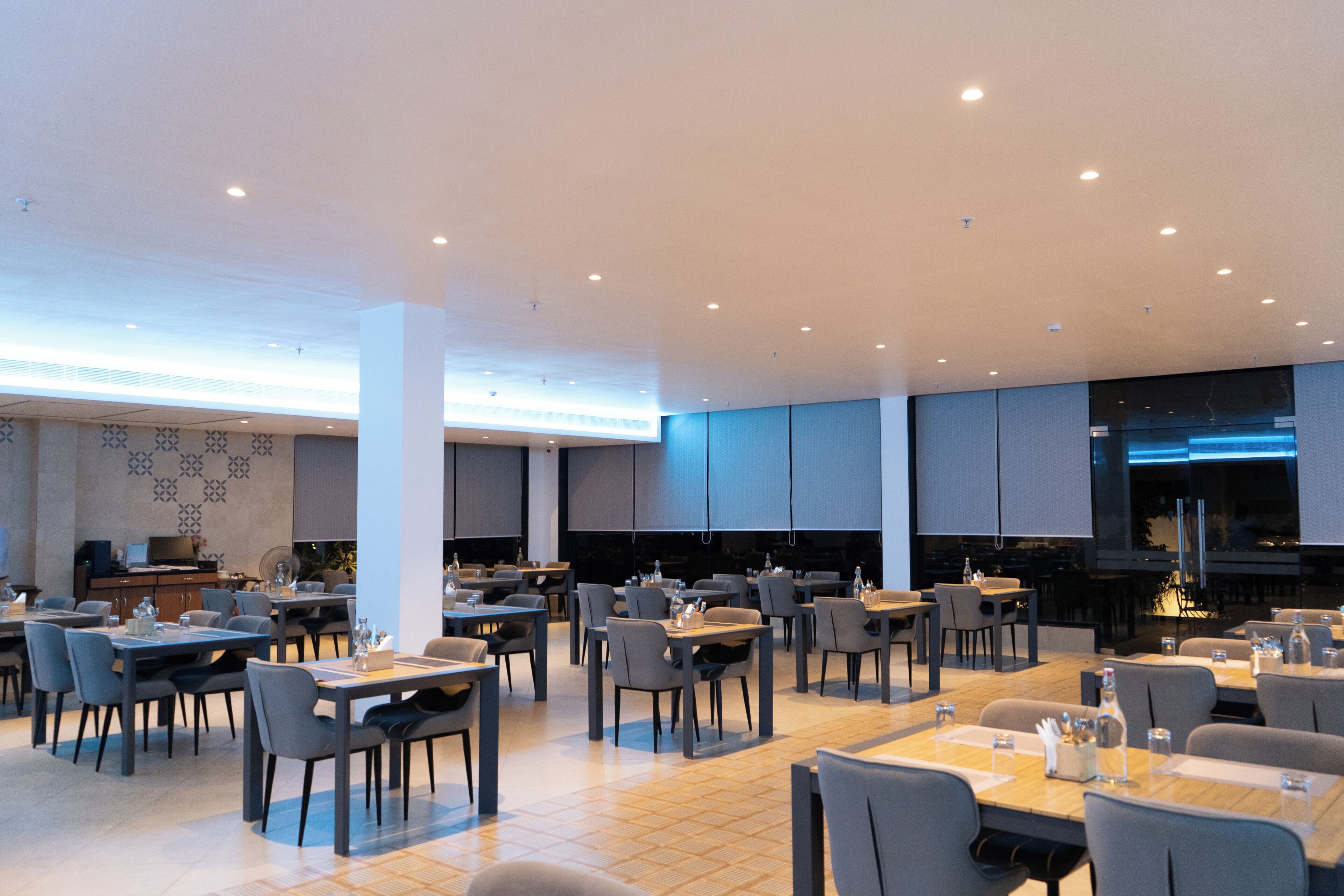 A modern dining area with multiple tables and chairs, a bar area, and a view of the cityscape.