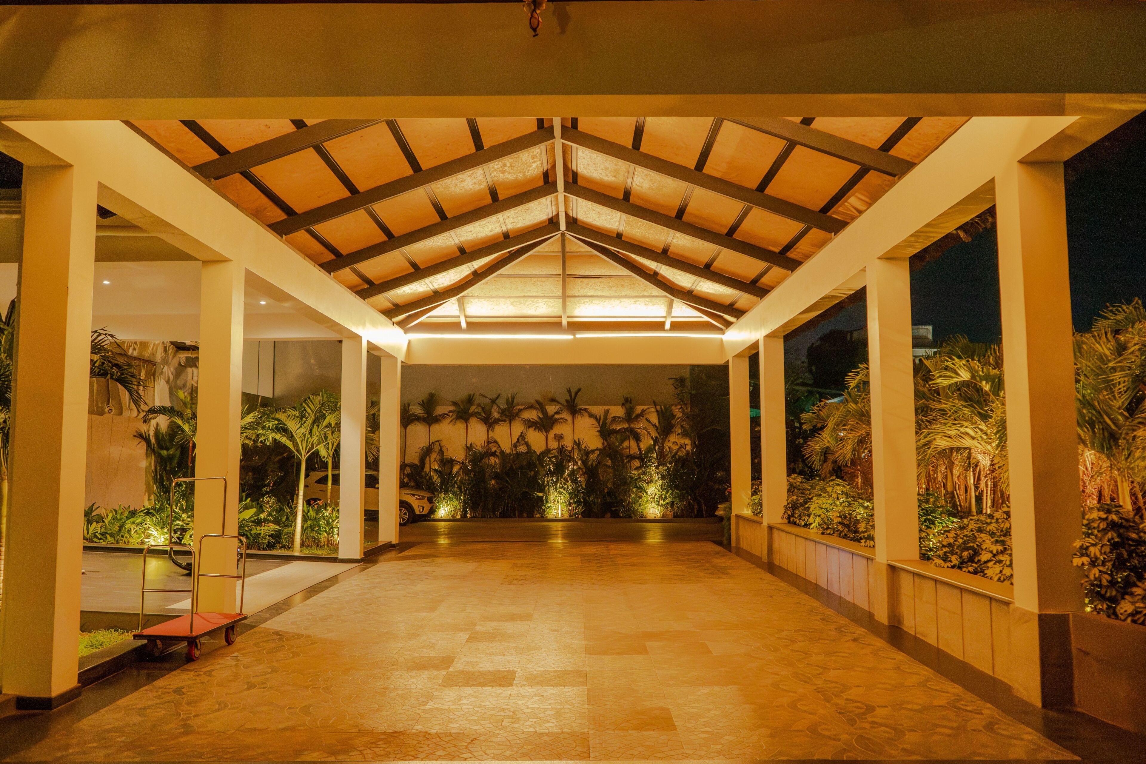 A covered outdoor area with a tiled floor, palm trees, and a ceiling with wooden beams.
