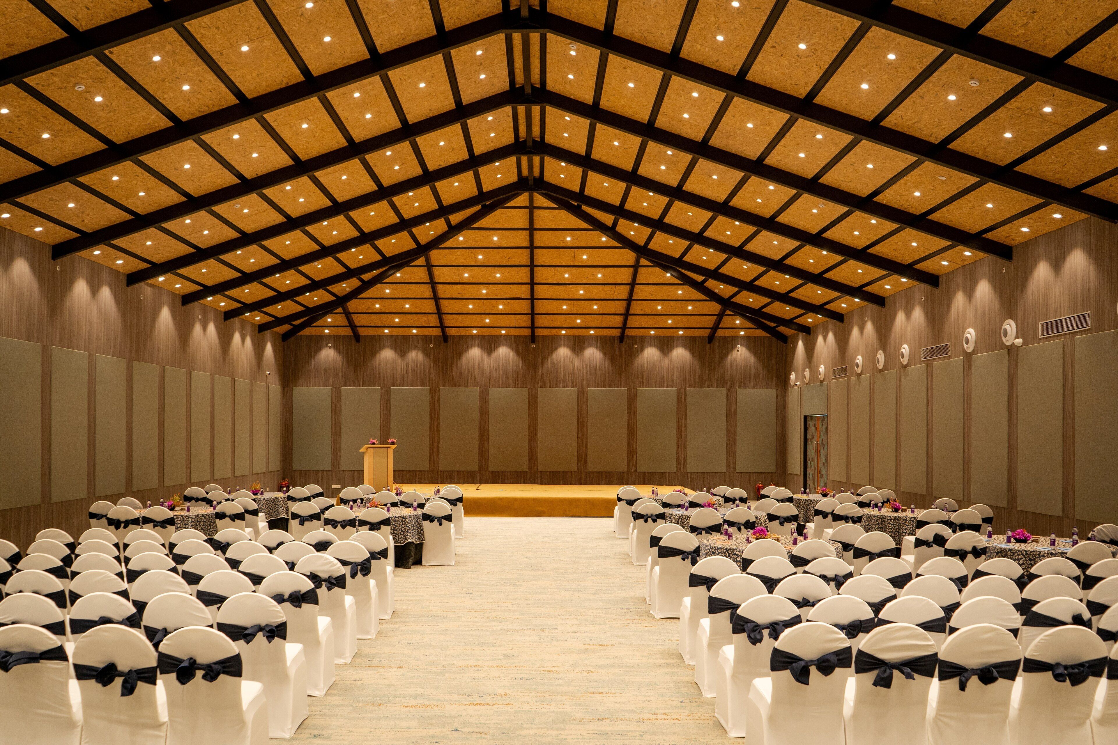 A large hall with rows of white chairs with black sashes, a podium at the front, and a high ceiling with wooden beams and recessed lighting.
