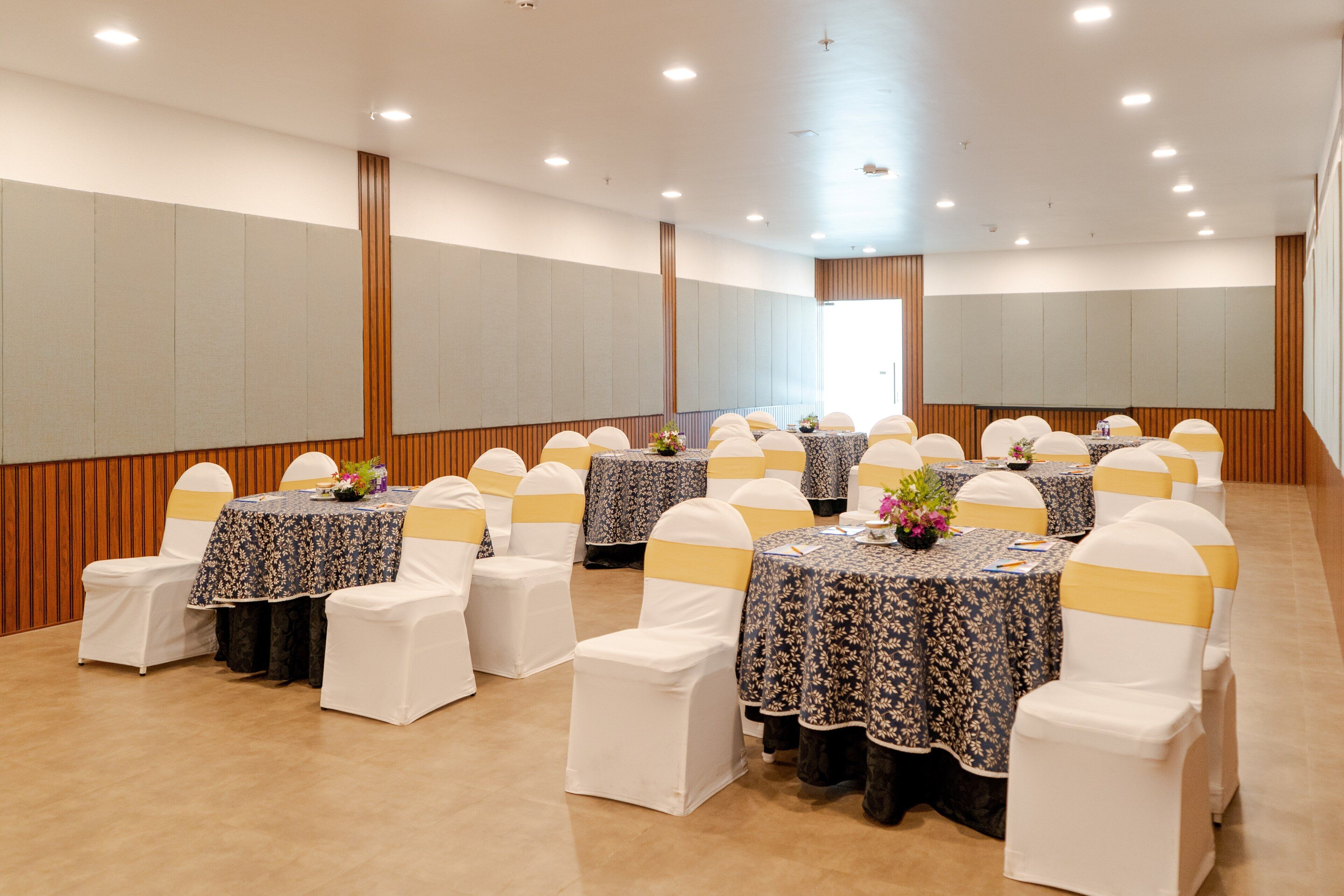 A conference room with round tables, white chairs with yellow sashes, and floral centerpieces.