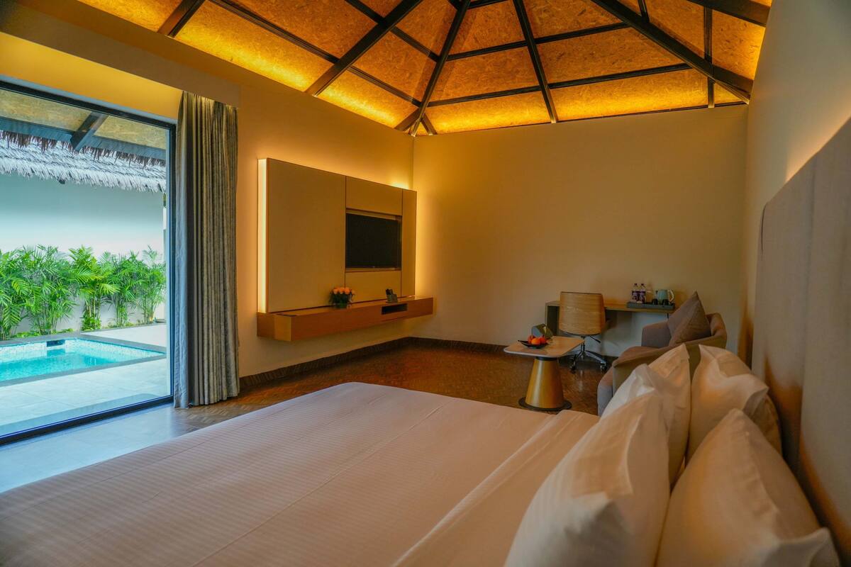 A hotel room with a large bed, a small table with a lamp, a mirror, and a view of a swimming pool.